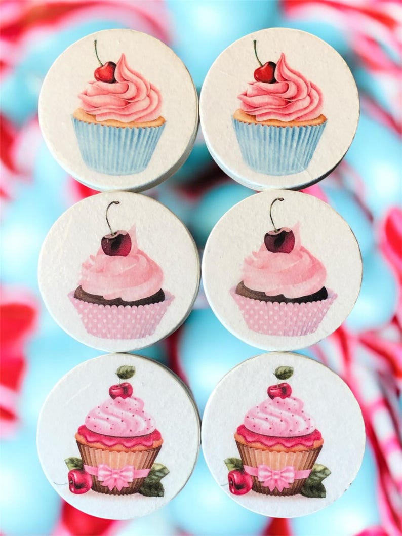 K&ouml;nnte beinhalten: Sechs runde Untersetzer mit Cupcake-Motiven. Jeder Untersetzer zeigt einen anderen Cupcake mit rosa Zuckerguss und einer Kirsche. Die Cupcakes befinden sich in blauen, rosa und braunen Papierf&ouml;rmchen. Der Hintergrund ist eine Mischung aus Blau und Rot.