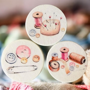 Könnte beinhalten: Aquarellillustrationen von Nähutensilien auf runden Untersetzern. Die Designs umfassen Garnrollen, ein Nadelkissen mit Nadeln, Knöpfe, eine Sicherheitsnadel und ein Maßband. Die Farbpalette umfasst sanfte Rosa-, Braun- und Cremetöne.