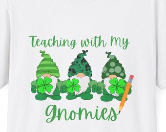 May include: White t-shirt featuring green gnomes wearing green hats and holding shamrocks. The text "Teaching with my Gnomes" is printed on the shirt.