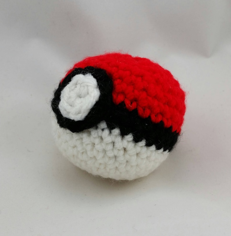 May include: A crocheted Pok&eacute; Ball with a red, white, and black design. The Pok&eacute; Ball is a popular item in the Pok&eacute;mon franchise.