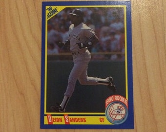 May include: A baseball card featuring Deion Sanders in a New York Yankees uniform. The card has a blue border with the text "90 SCORE" and "1990 ROOKIE". Sanders is depicted running, with the Yankees logo visible.