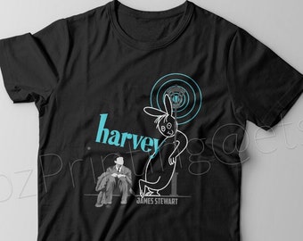 Könnte beinhalten: Schwarzes T-Shirt mit einer blauen und weißen Illustration eines Kaninchens und eines sitzenden Mannes. Der Text "harvey" ist in blau und der Text "JAMES STEWART" in weiß geschrieben.