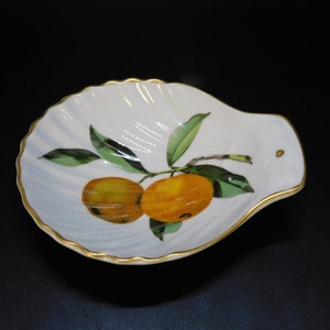May include: A white ceramic serving dish shaped like a seashell with a gold rim. The dish features a painted design of two oranges on a branch with green leaves.