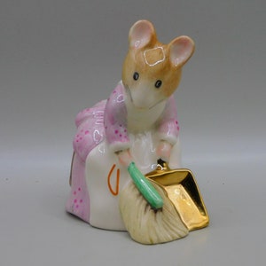 Może przedstawiać: Porcelanowa figurka myszy w różowej sukience i fartuchu, trzymająca zielony miotłę i złotą szufelkę.