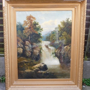 May include: A framed oil painting depicting a waterfall cascading through a rocky landscape. Lush green trees and foliage surround the waterfall, creating a serene and picturesque scene.