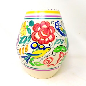 May include: A cream-coloured ceramic vase featuring a hand-painted folk art design. The pattern includes a large red flower, a yellow bird, green leaves, and blue accents. Horizontal yellow, purple, and teal bands encircle the top and bottom.