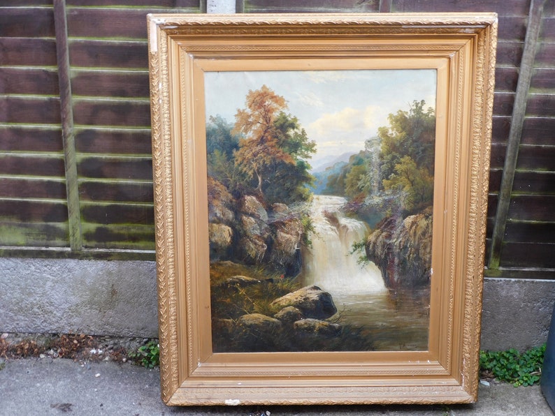 May include: A framed oil painting depicting a waterfall cascading through a rocky landscape. Lush green trees and foliage surround the waterfall, creating a serene and picturesque scene.