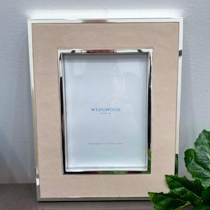 May include: A rectangular picture frame with a silver metal border and a light tan suede-like insert. The frame has the word "WEDGWOOD" printed on the inside. The picture size is 5" x 7" / 12.5cm x 17.8cm.
