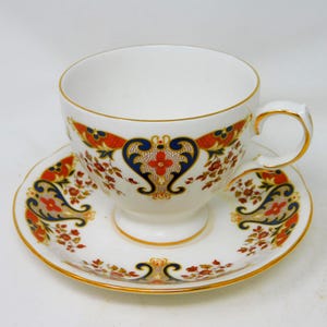 Peut inclure: Service à thé blanc composé d'une tasse et d'une soucoupe ornées de motifs floraux et de volutes rouges, bleus et dorés. La tasse et la soucoupe ont des bords dorés. Un service à thé classique.