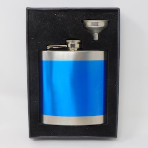 Könnte beinhalten: Eine Edelstahl-Flachmann mit einem leuchtend blauen Mittelband, präsentiert in einer schwarzen Geschenkbox. Der Flachmann enthält einen kleinen silbernen Trichter. Der Flachmann ist etwa 10 cm hoch.