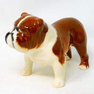 May include: A ceramic bulldog figurine in a standing pose. The dog has a glossy finish with brown and white markings. The bulldog's face is detailed with black accents, and it has a determined expression.