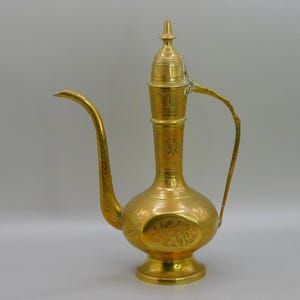 Peut inclure: Une théière en laiton de couleur dorée avec des motifs gravés complexes. La théière a un corps haut et mince avec une base arrondie et un bec qui s'incurve vers le haut. Le couvercle est bombé et possède un bouton sur le dessus.