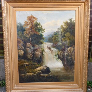 May include: A framed oil painting depicting a waterfall cascading through a rocky landscape. Lush green trees and foliage surround the waterfall, creating a serene and picturesque scene.