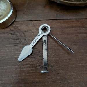 May include: A silver-colored metal pipe tool featuring three folding implements: a tamper, a reamer, and a pick. The central pivot point is stamped with the text MADE IN U.S.A. and the text HALF AND HALF is clearly visible on the reamer blade.