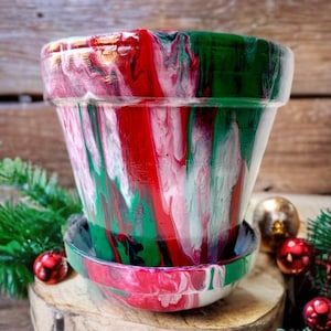 May include: A red, green, and white terra cotta planter with a matching saucer. The planter has a swirled, abstract design.