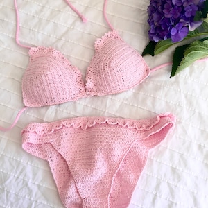 May include: A pink crocheted bikini set with a triangle top and a high-waisted bottom. The bikini has a delicate crochet trim.