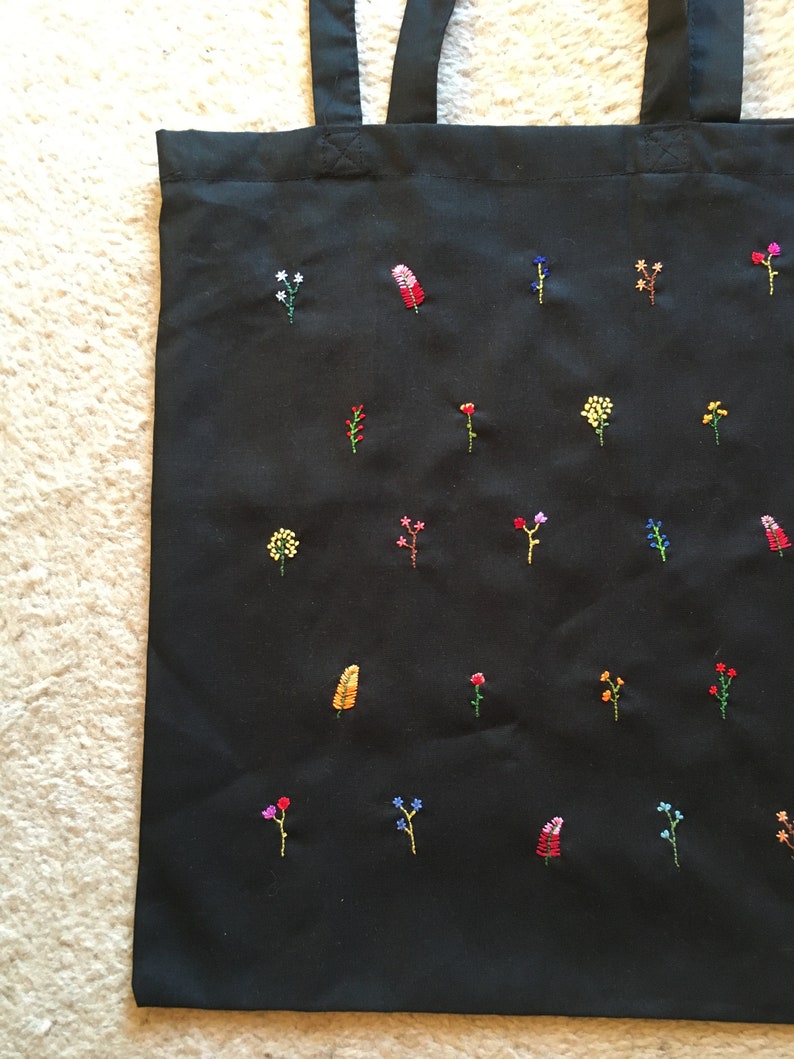 以下が含まれることがあります： カラフルな刺繍の花と葉がついた黒いトートバッグ