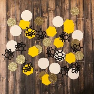 May include: A collection of yellow and black bee-themed confetti. The confetti includes bees, honeycombs, and polka dots.