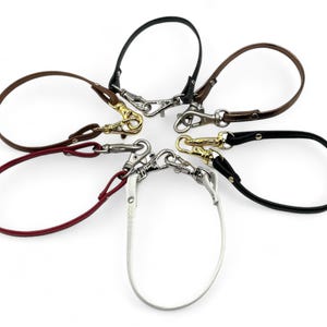 May include: A selection of leather wrist straps in colours such as black, brown, and burgundy. Each strap has a metal clasp. The straps are arranged in a circular pattern against a white background.