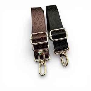 May include: Two adjustable purse straps. One strap is brown with a repeating diamond pattern, the other is black with a similar pattern. Both straps have gold-colored metal hardware, including rectangular buckles and swivel clasps.