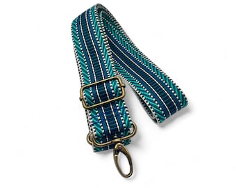 May include: A blue and green patterned adjustable strap with a brass buckle and clasp. The strap is made of woven fabric and is suitable for bags or purses.