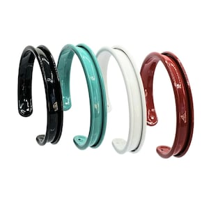 May include: Four different colored bangle bracelets. The bracelets are made of a smooth, glossy material. The colors are black, teal, white, and red.