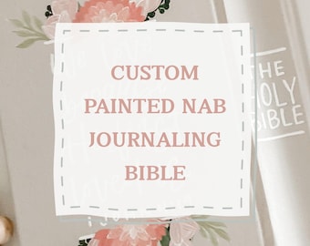 Pode incluir: Uma Bíblia de journaling cinza-claro com ilustrações florais pintadas à mão em tons de rosa e coral na capa. O texto CUSTOM PAINTED NAB JOURNALING BIBLE está centralizado numa caixa branca com linhas tracejadas sobre o design floral.