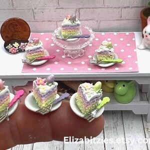 May include: A set of five miniature cakes decorated with pastel frosting and colorful sprinkles. The cakes are displayed on small plates with forks. The cakes are arranged on a white table with a pink and white polka dot tablecloth.
