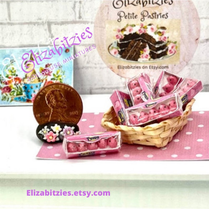 May include: A miniature dollhouse-sized basket filled with pink Peeps marshmallow candies. The basket is on a pink and white polka dot surface. A miniature penny coin is on the left side of the image. The text "Elizabitzies on Etsy.com" is on a sign in the background.