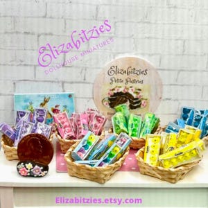 May include: A miniature dollhouse bakery display with various pastel-colored candy eggs in small wicker baskets. The sign reads "Elizabitzies Petite Pastries".