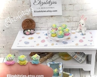 May include: A miniature Easter scene with yellow chicks on cupcakes, a plate of cupcakes, and a white bunny. The cupcakes are decorated with green grass and yellow chicks. The scene is set on a white table with a pink and white checkered tablecloth. The text "Elizabitzies.etsy.com" is visible in the image.