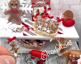 May include: A miniature Christmas scene with gingerbread cookies, a gingerbread man, a red and white candy cane basket, a red stand mixer, and a reindeer figurine. The scene is set on a white table with red and white striped paper.