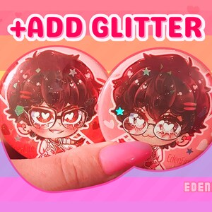 Op de afbeelding: Twee rode en roze knoopsluitingen met een cartoonfiguur dat een bril en een wit shirt draagt. Het personage heeft bruin haar en hartvormige ogen. De knoopsluitingen hebben glitter in het ontwerp ingebed. De tekst "ADD GLITTER" staat bovenaan de afbeelding en de tekst "EDENFIRE" staat onderaan de afbeelding.