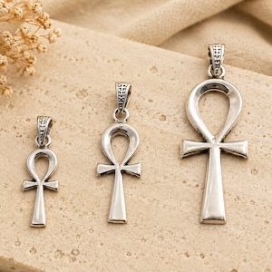 May include: Three silver-toned ankh pendants of varying sizes arranged in a row. Each pendant features a classic looped cross design with a textured bail at the top, showcasing a polished metallic finish and a distinct Egyptian symbol shape.