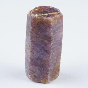 May include: A rough cut gemstone with a hexagonal shape, featuring purple and brown hues.