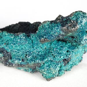 May include: A close-up of a mineral specimen with a textured surface. The mineral displays a vibrant teal colour with areas of black and dark blue. The crystalline structure is visible, creating a rough, uneven appearance.