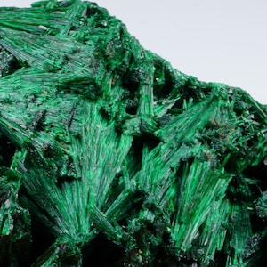 Op de afbeelding: Een cluster van levendige groene malachietkristallen, met een vezelachtige textuur, die een natuurlijke rotsformatie vormen.