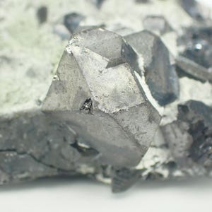 May include: Detailed image of a mineral specimen with a prominent, metallic grey crystal. The crystal displays sharp, geometric facets and is set within a matrix of lighter grey and white. The texture is rough and uneven.