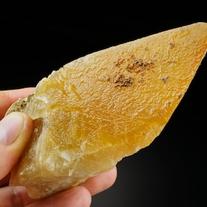 Puede incluir: Un gran cristal de calcita amarillo translúcido con una superficie rugosa y texturizada. El cristal tiene forma de cuña puntiaguda y afilada.