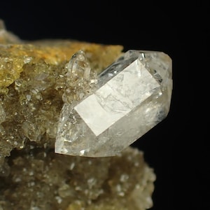 Peut inclure: Gros plan sur une formation de cristaux de quartz clair. Le cristal est d'une couleur claire et translucide avec une forme géométrique. Il est placé sur un fond d'autres cristaux plus petits et un fond sombre.