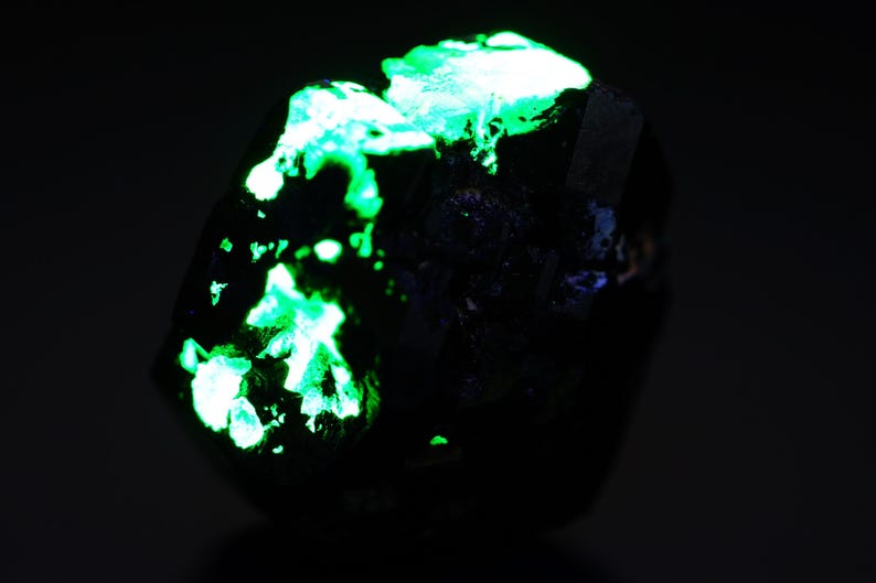 May include: A dark, irregularly shaped mineral specimen with bright, glowing green patches. The contrast between the dark base and the vibrant green highlights the unique texture and crystalline structure of the rock. The image is set against a dark background.