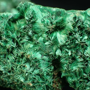 Op de afbeelding: Close-up van een levendig groen malachiet mineraal specimen. Het oppervlak is bedekt met een dichte cluster van stralende, naaldachtige kristallen, waardoor een getextureerde, opvallende weergave ontstaat. De kleur varieert van heldergroen tot diepgroen.