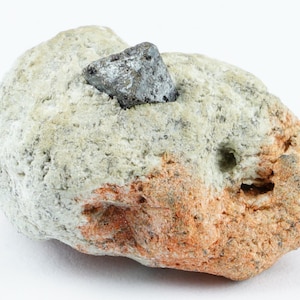 May include: A dark grey, octahedral crystal of haematite embedded in a light grey and orange rock.