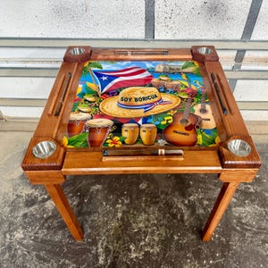 May include: A wooden domino table with a colorful, artistic design featuring the Puerto Rican flag, musical instruments, and the words "SOY BORICUA" on a straw hat. The table has four cup holders and slots for dominoes.