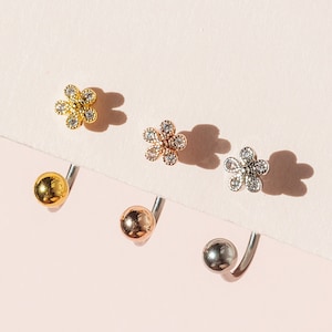 Peut inclure: Trois paires de boucles d'oreilles en or, or rose et argent. Chaque paire comprend un petit clou de fleur avec des cristaux clairs et une barre incurvée avec une boule à l'extrémité. Les boucles d'oreilles sont présentées sur une surface rose clair.