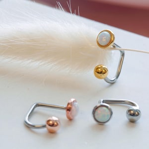 May include: Three surgical steel body jewelry pieces with opal stones. The jewelry is in gold, rose gold, and silver tones.