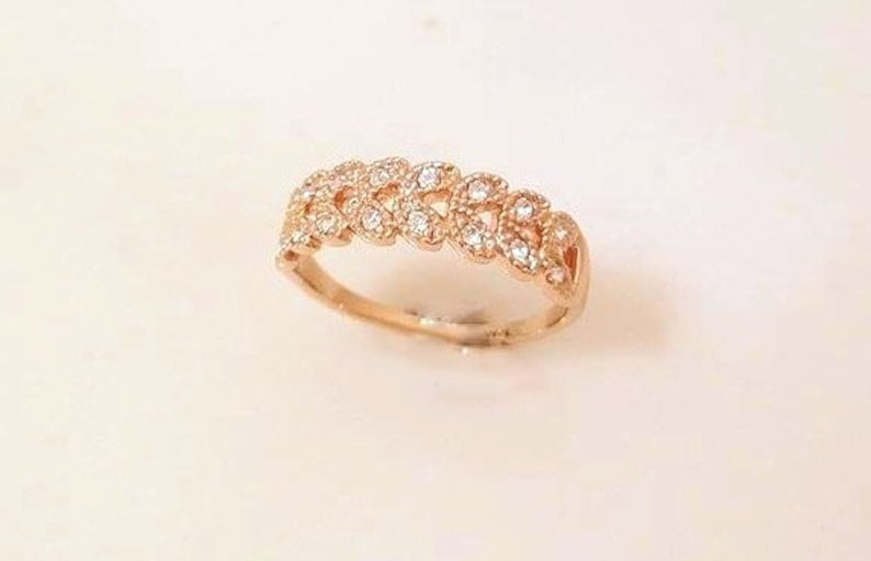 May include: A rose gold ring with a floral design. The ring features a series of connected, leaf-like shapes, each adorned with small, clear gemstones. The band is smooth and polished, creating a contrast with the textured top.