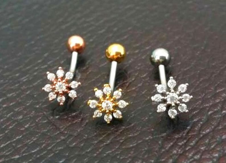 Puede incluir: Tres piercings para el ombligo con dise&ntilde;o de flor. Uno es de oro rosa con piedras transparentes, otro es dorado con piedras transparentes y otro es plateado con piedras transparentes. Cada uno tiene una bola en la parte superior.