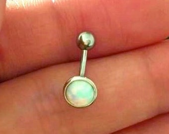 May include: A belly button ring with a silver-colored post and two rounded ends. The bottom end features a round, opalescent stone set in a silver bezel. The top end is a small, silver ball.