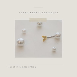 May include: A gold-colored, arrow-shaped earring with a pearl back, and several white pearl earrings. The text "PEARL BACKS AVAILABLE" is at the top of the image. The text "LINK IN ITEM DESCRIPTION" is at the bottom of the image.